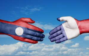 Mains peintes aux couleurs des drapeaux du Laos et de la France se serrant sur fond de ciel, symbolisant la coopération internationale et l’implantation d’entreprises européennes en Asie du Sud-Est.