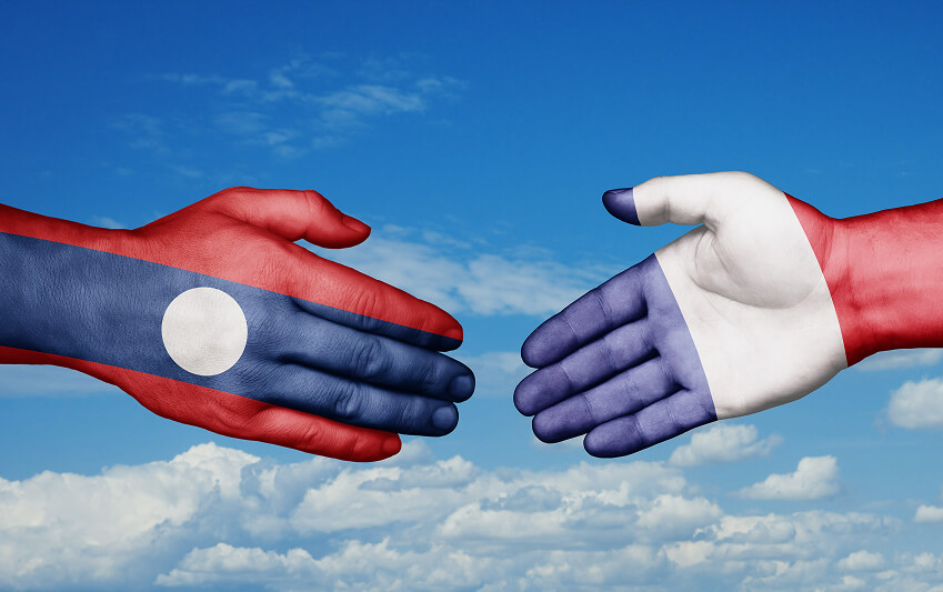 Mains peintes aux couleurs des drapeaux du Laos et de la France se serrant sur fond de ciel, symbolisant la coopération internationale et l’implantation d’entreprises européennes en Asie du Sud-Est.